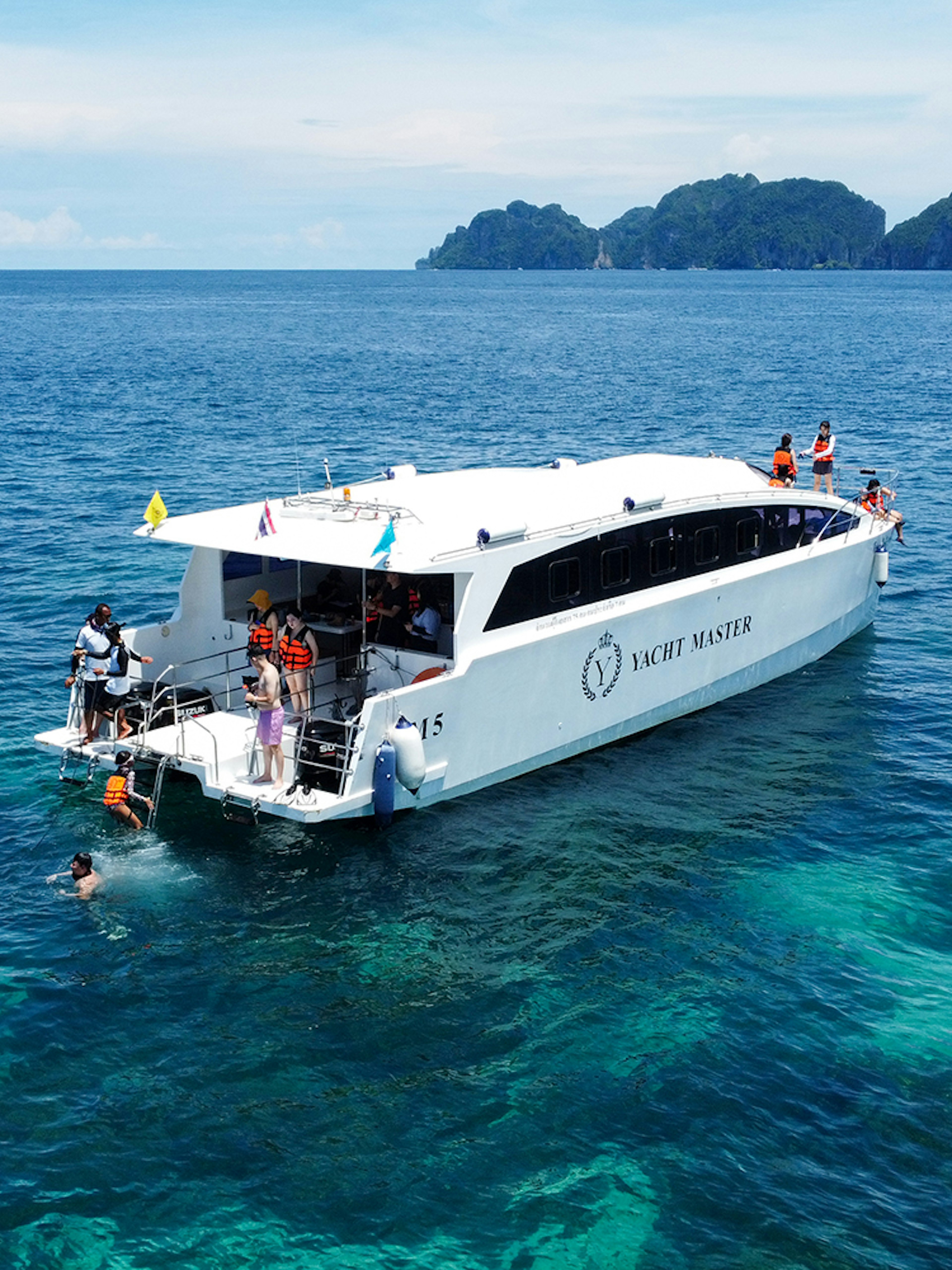Speed catamaran near Phi Phi Island with tourists snorkeling in clear blue water.