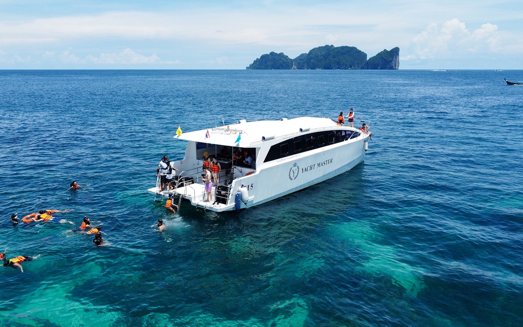 Speed catamaran near Phi Phi Island with tourists snorkeling in clear blue water.