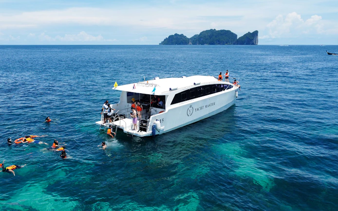 Speed catamaran near Phi Phi Island with tourists snorkeling in clear blue water.