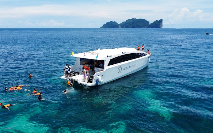 Speed catamaran near Phi Phi Island with tourists snorkeling in clear blue water.