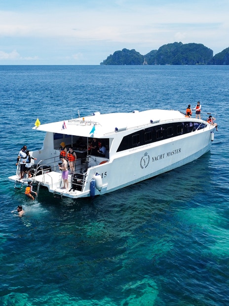Speed catamaran near Phi Phi Island with tourists snorkeling in clear blue water.