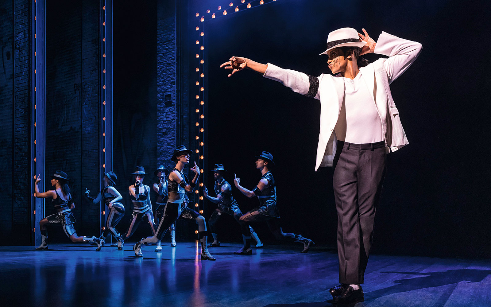 Performer in white suit and hat dancing on stage with backup dancers in MJ Das Musical.