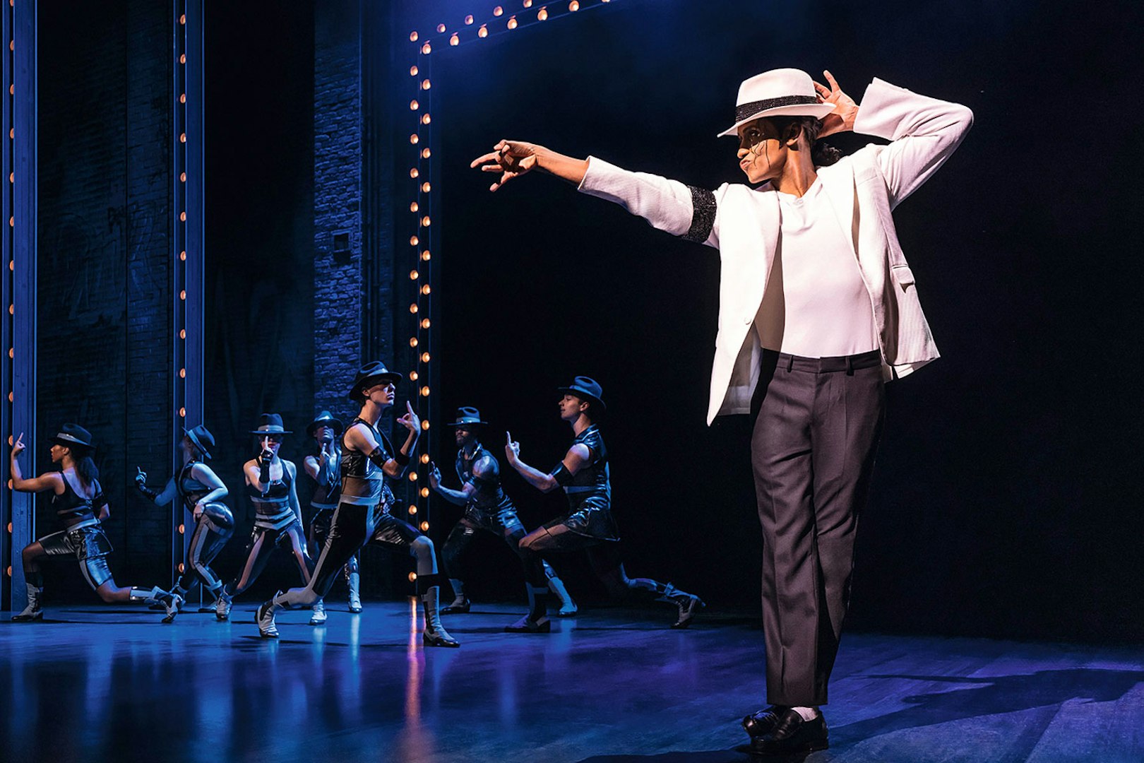 Performer in white suit and hat dancing on stage with backup dancers in MJ Das Musical.