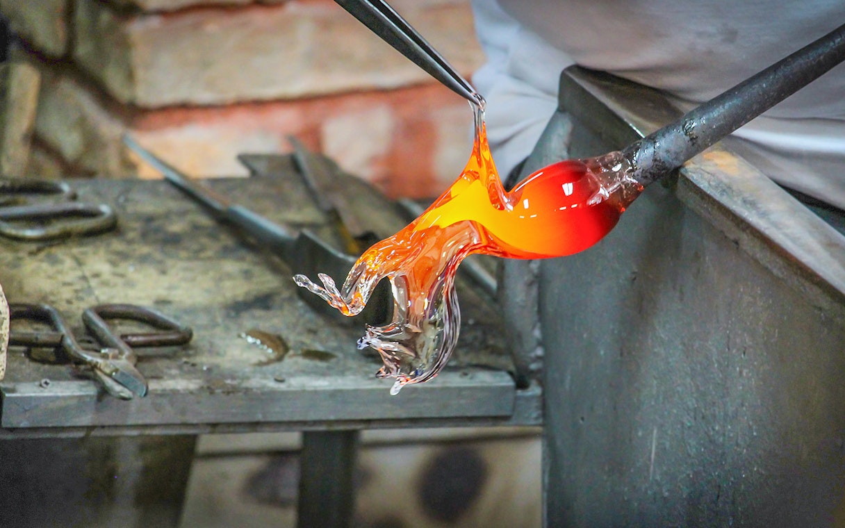 Glass artist shaping molten glass in Murano workshop.