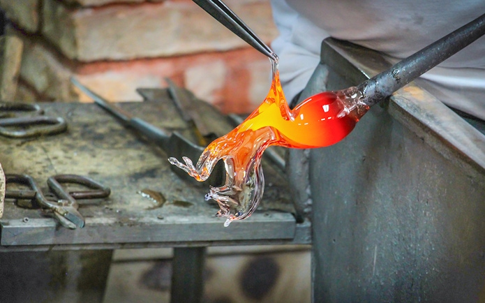 Glass artist shaping molten glass in Murano workshop.