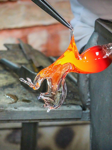 Glass artist shaping molten glass in Murano workshop.