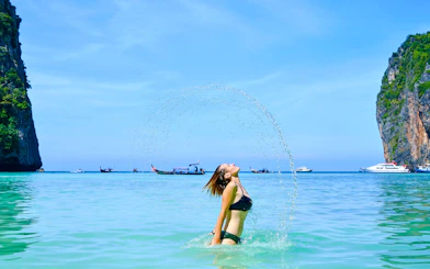 Tourist enjoying a swim at Phi Phi Island beach with boats and cliffs in the background.