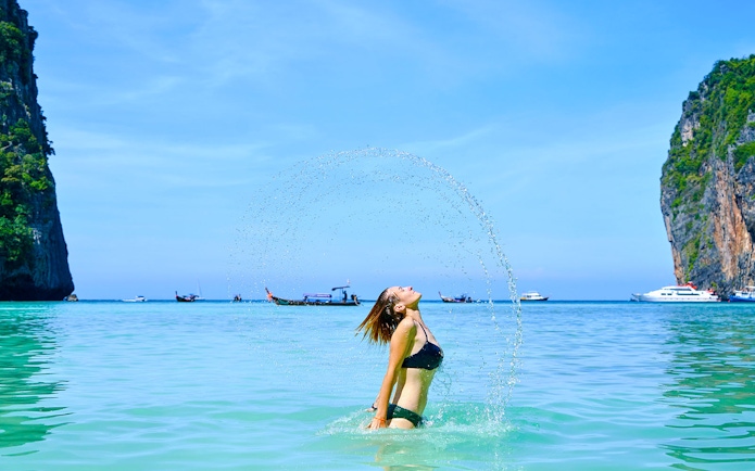 Tourist enjoying a swim at Phi Phi Island beach with boats and cliffs in the background.