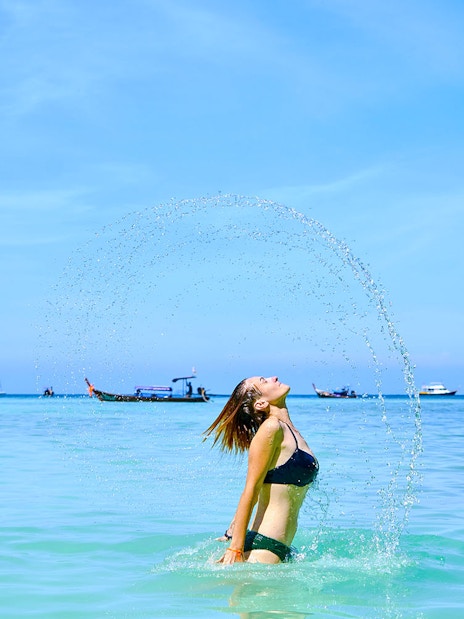 Tourist enjoying a swim at Phi Phi Island beach with boats and cliffs in the background.