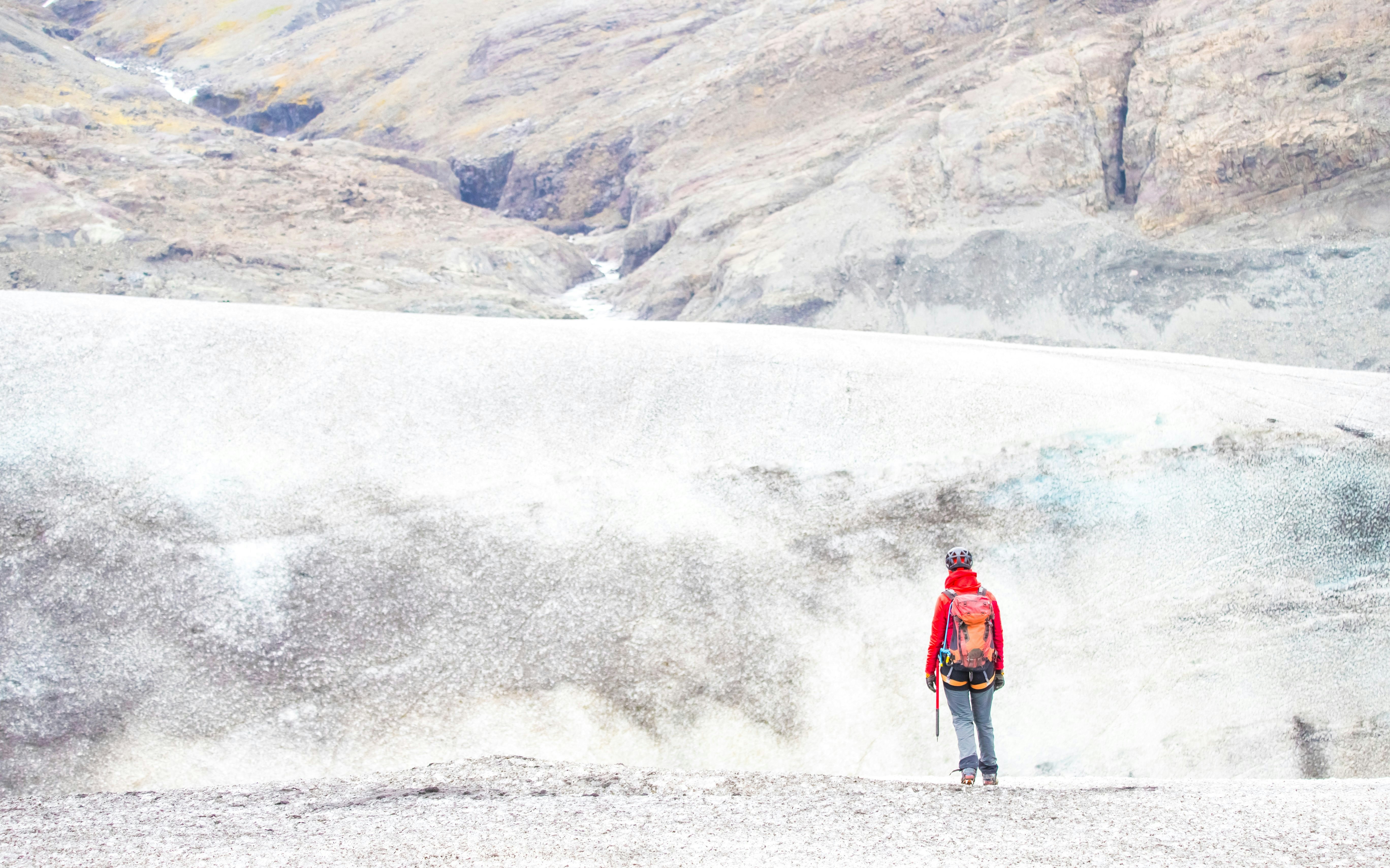 Person standing at Falljokull Glacier edge viewpoint, Iceland, with rocky terrain in the background.