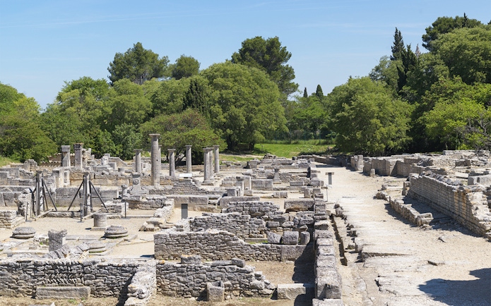 Glanum Archaeological Site ruins with stone columns and ancient structures in a green landscape.