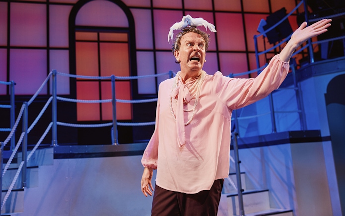 Performer on stage in Titanique musical with ship backdrop.