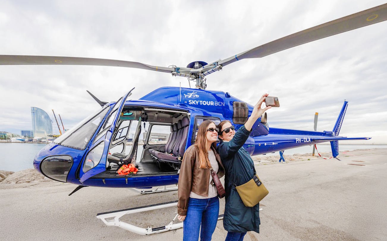 Tourists taking a selfie near a blue helicopter in Barcelona.