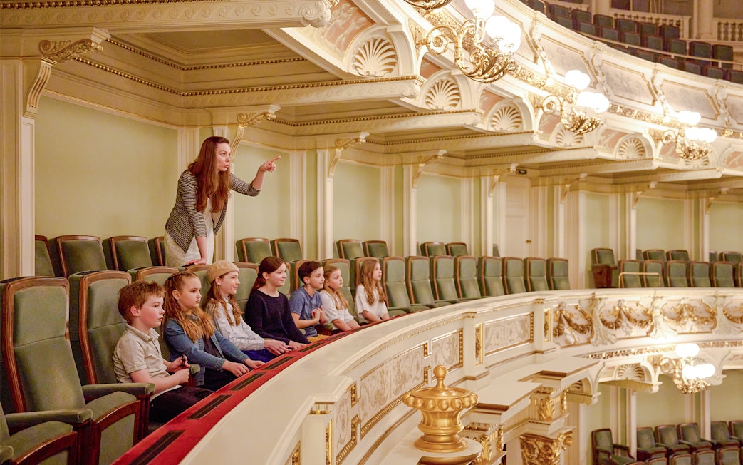 Guide pointing out features to children in an ornate theater balcony.