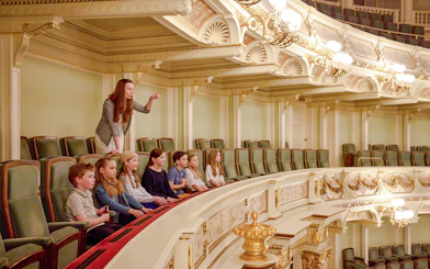 Guide pointing out features to children in an ornate theater balcony.