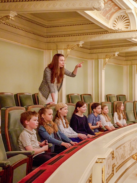 Guide pointing out features to children in an ornate theater balcony.