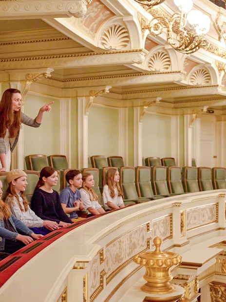 Guide pointing out features to children in an ornate theater balcony.