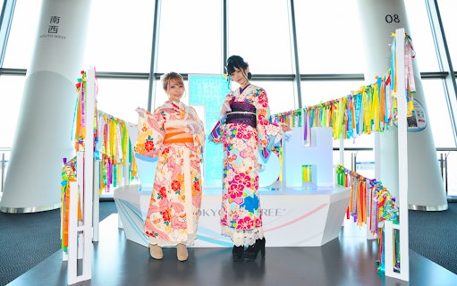 Two people in colorful kimonos at Tokyo Skytree observation deck.