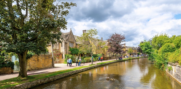 Riverside path with people walking in Bourton-on-the-Water, Cotswolds.