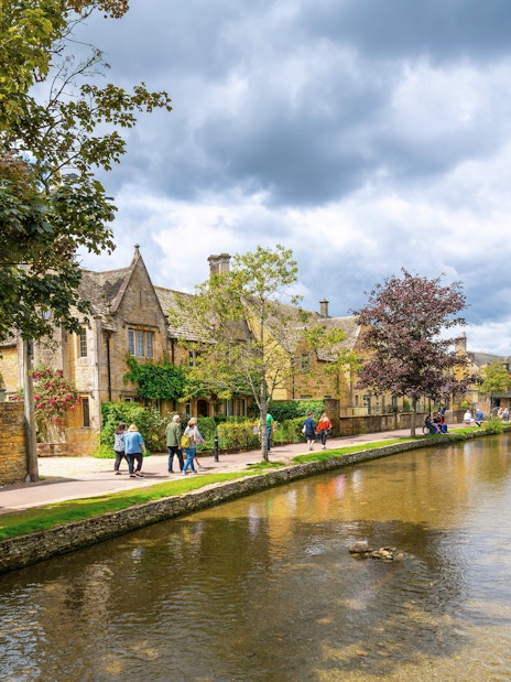 Riverside path with people walking in Bourton-on-the-Water, Cotswolds.