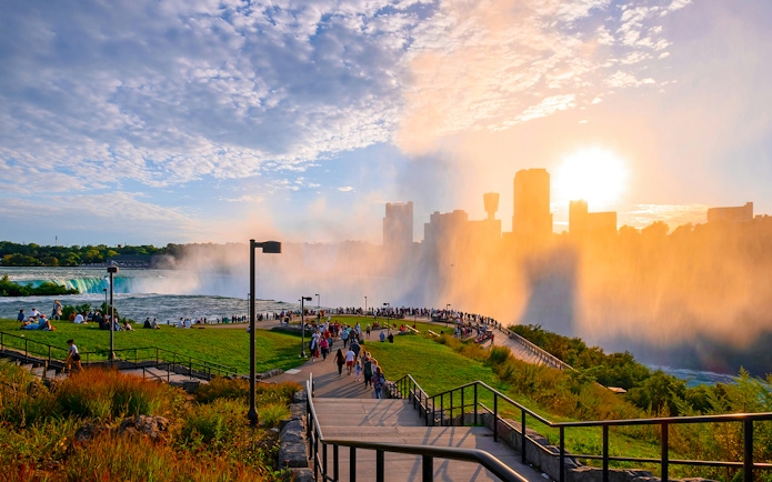 Visitors at Terrapin Point overlooking Niagara Falls, New York, with mist and city skyline in the background.