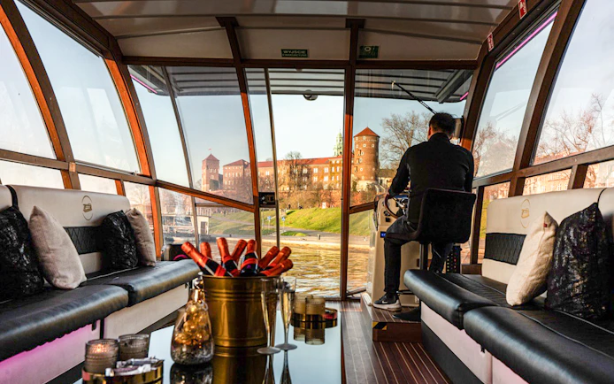 Interior view of a catamaran on the Vistula River Cruise in Krakow, with Wawel Castle visible through the windows.