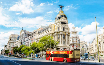 Big Bus Madrid passing by the Metropolis Building on a sunny day.