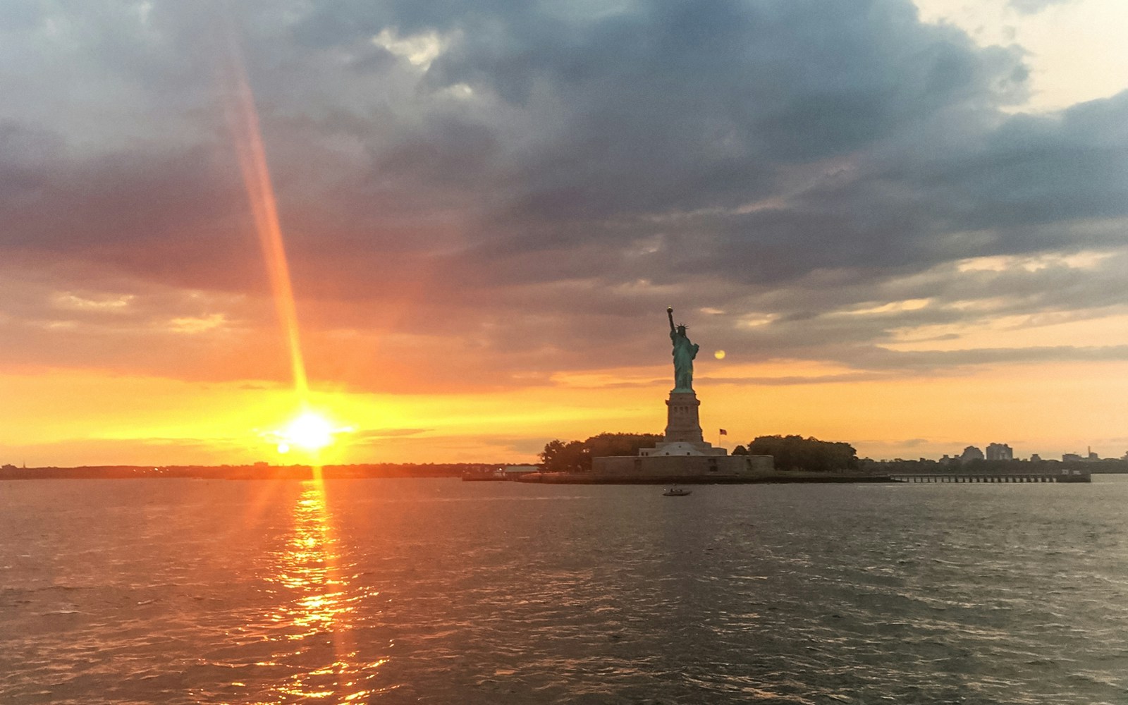 Statue of Liberty and Ellis Island at sunset during a scenic cruise in New York Harbor.