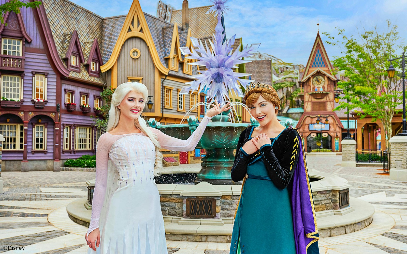 Anna and Elsa posing in front of a themed village at Disneyland Hong Kong's Frozen Ever After attraction.