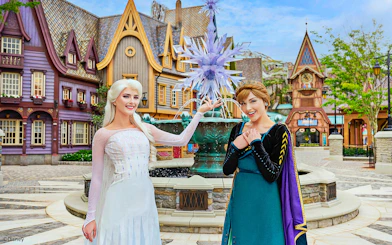Anna and Elsa posing in front of a themed village at Disneyland Hong Kong's Frozen Ever After attraction.