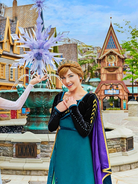 Anna and Elsa posing in front of a themed village at Disneyland Hong Kong's Frozen Ever After attraction.