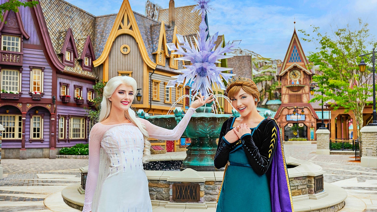 Anna and Elsa posing in front of a themed village at Disneyland Hong Kong's Frozen Ever After attraction.