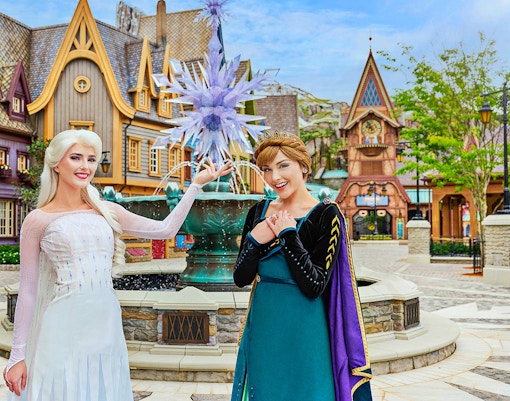 Anna and Elsa posing in front of a themed village at Disneyland Hong Kong's Frozen Ever After attraction.