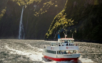 Cruise boat on Milford Sound with waterfall and lush cliffs in background, New Zealand.