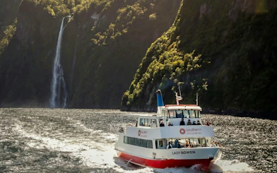 Cruise boat on Milford Sound with waterfall and lush cliffs in background, New Zealand.