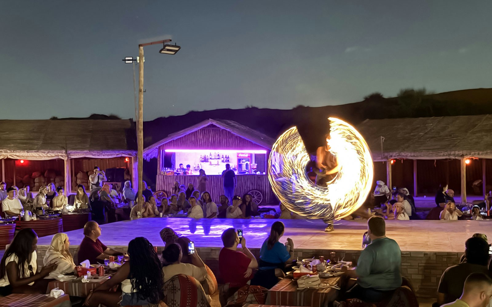 Fire performer spinning flames at a Dubai desert show with an audience watching.