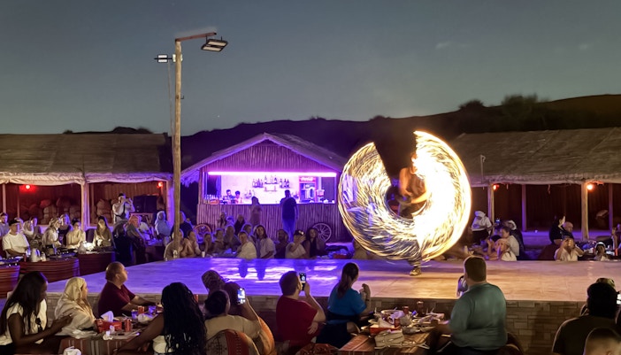Fire performer spinning flames at a Dubai desert show with an audience watching.