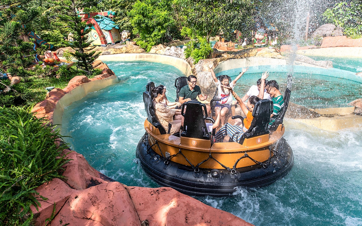 Guests on a water ride at VinWonders, surrounded by lush greenery and themed structures.