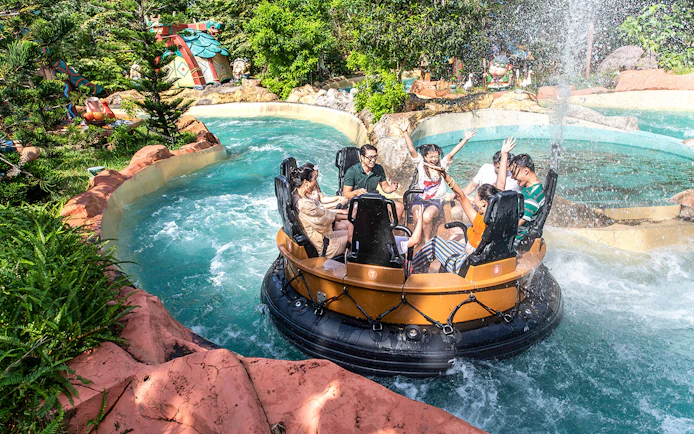 Guests on a water ride at VinWonders, surrounded by lush greenery and themed structures.
