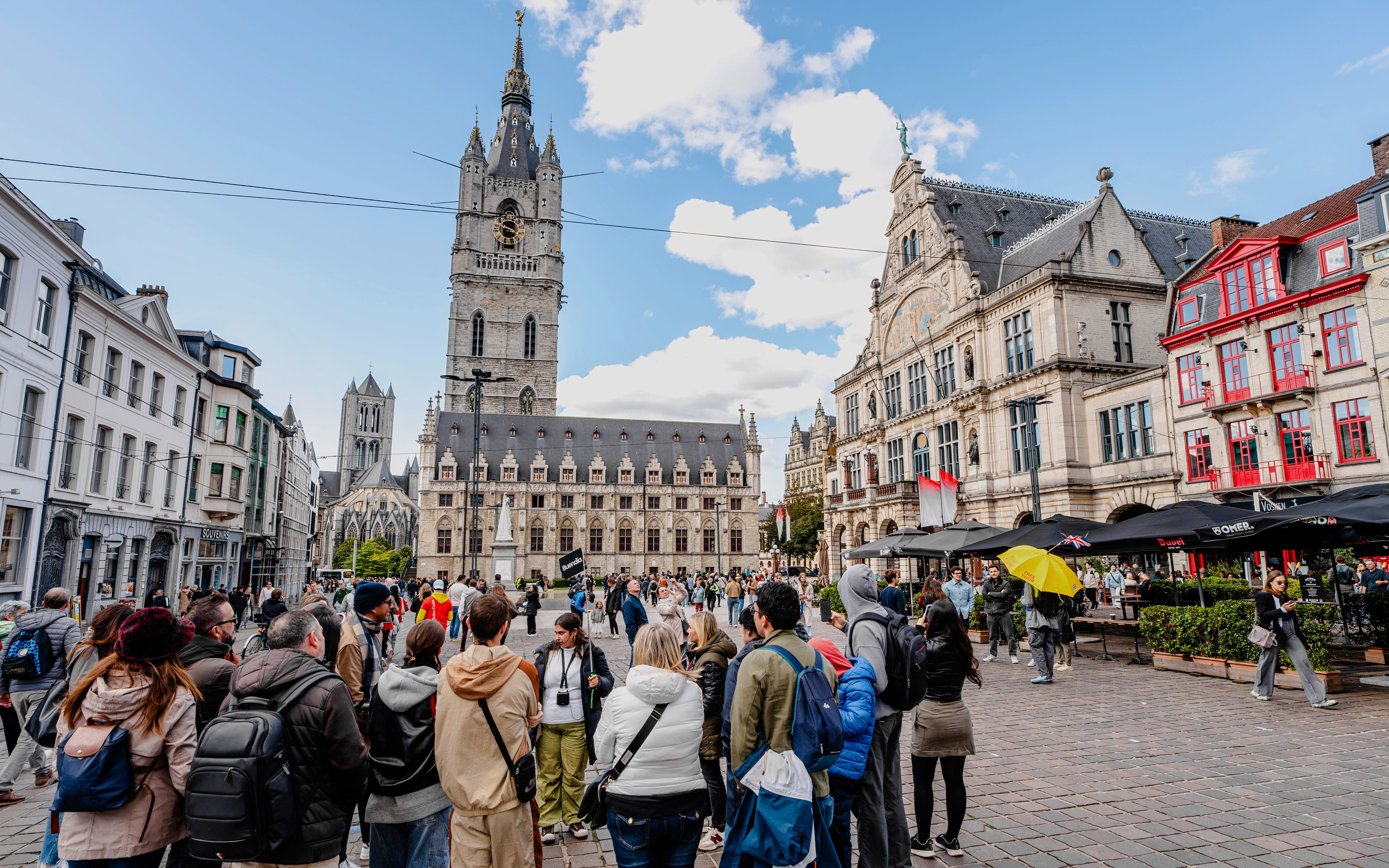 Tourists gathered in Sint-Baafsplein, Ghent, with the Belfry of Ghent in the background.
