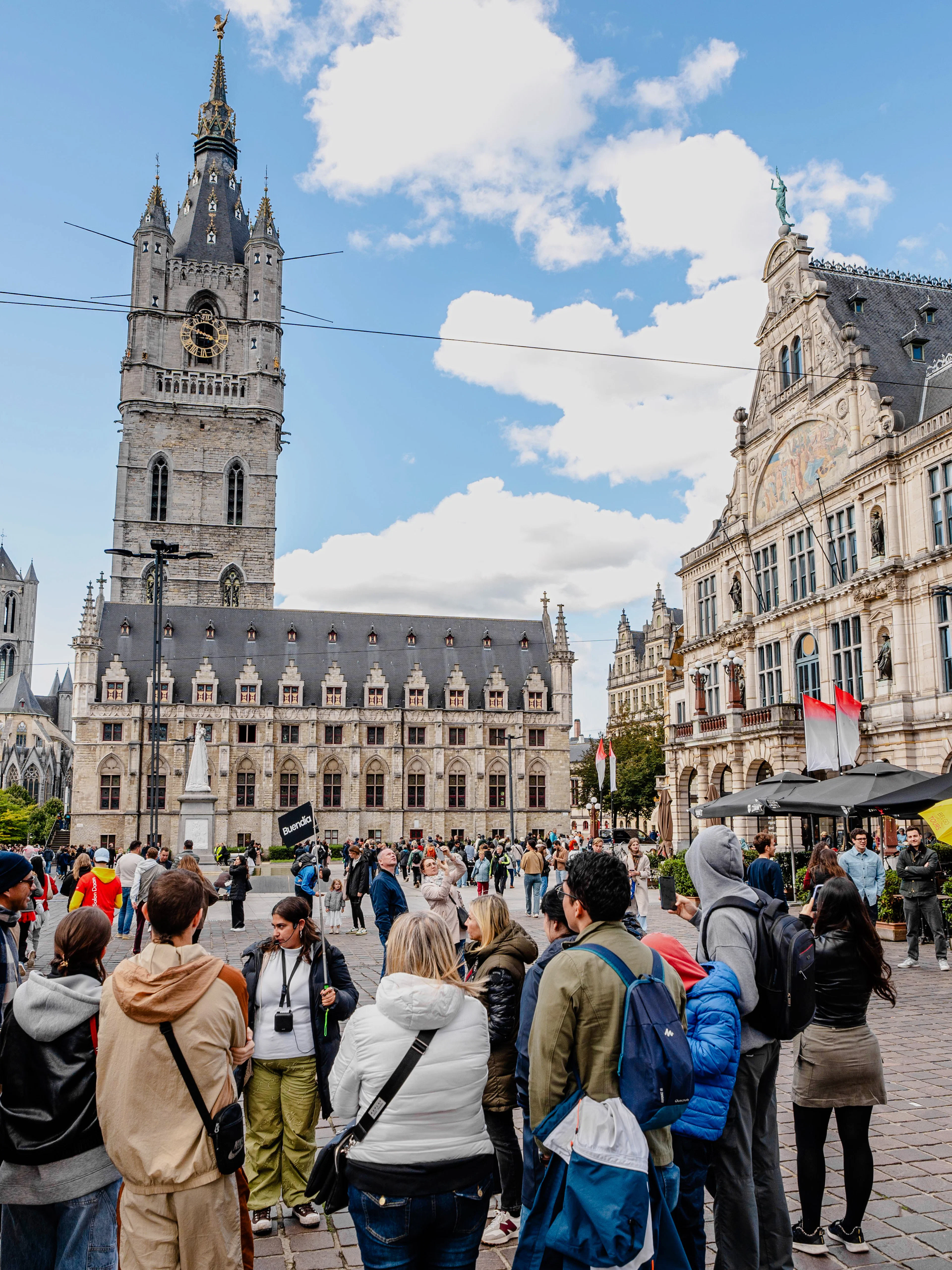 Tourists gathered in Sint-Baafsplein, Ghent, with the Belfry of Ghent in the background.