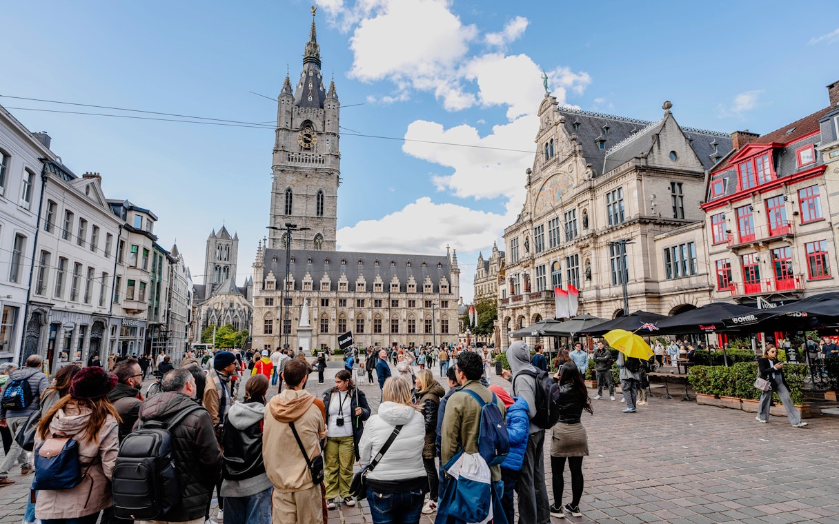 Tourists gathered in Sint-Baafsplein, Ghent, with the Belfry of Ghent in the background.