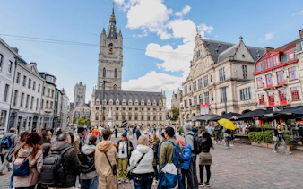 Tourists gathered in Sint-Baafsplein, Ghent, with the Belfry of Ghent in the background.
