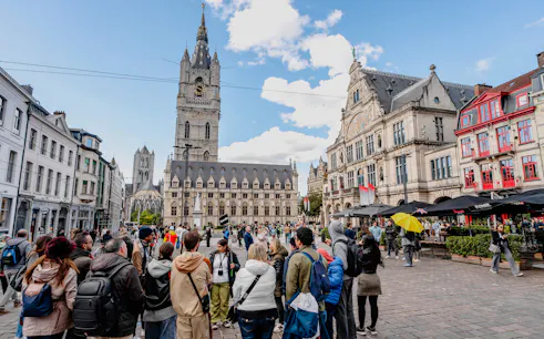 Tourists gathered in Sint-Baafsplein, Ghent, with the Belfry of Ghent in the background.