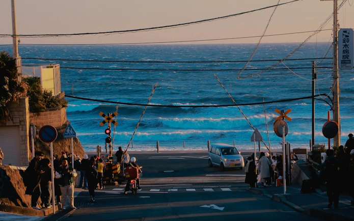 Coastal view from Enoden Train crossing in Kamakura, Japan, with ocean waves and people nearby.