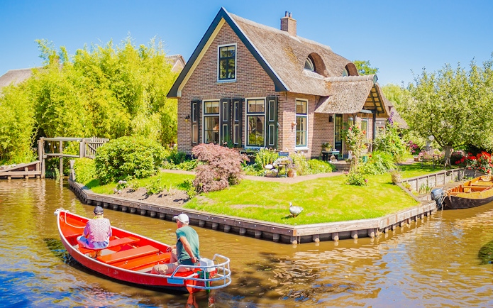 Small electric boat on canal near traditional house in Giethoorn, Netherlands.