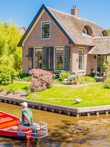 Small electric boat on canal near traditional house in Giethoorn, Netherlands.