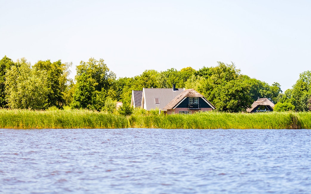 Giethoorn canal view with traditional houses and lush greenery.