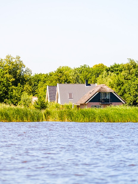 Giethoorn canal view with traditional houses and lush greenery.