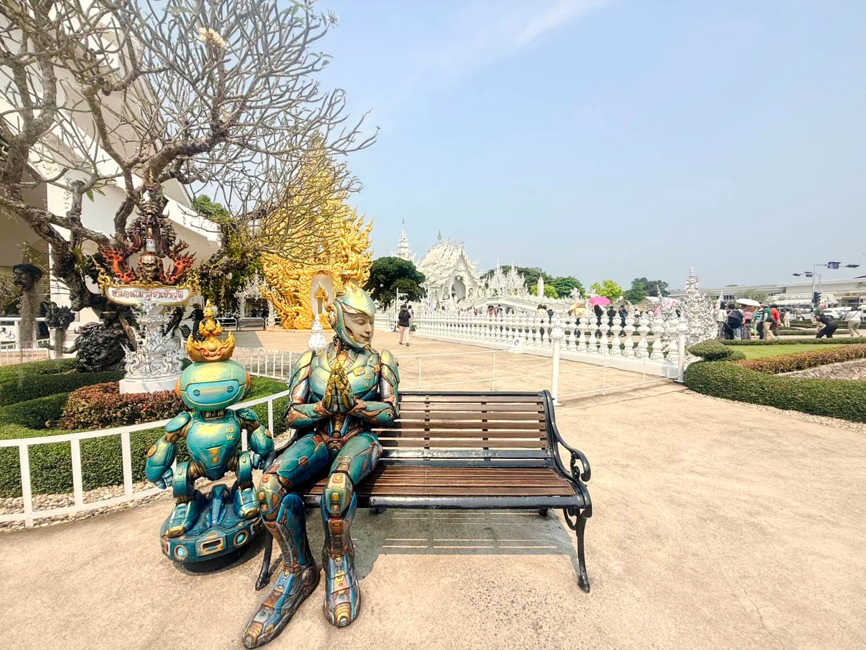 Robotic statues near White Temple, Chiang Rai, with intricate architecture in the background.